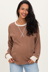 woman wearing a brown maternity pullover with white trim and a visible baby bump