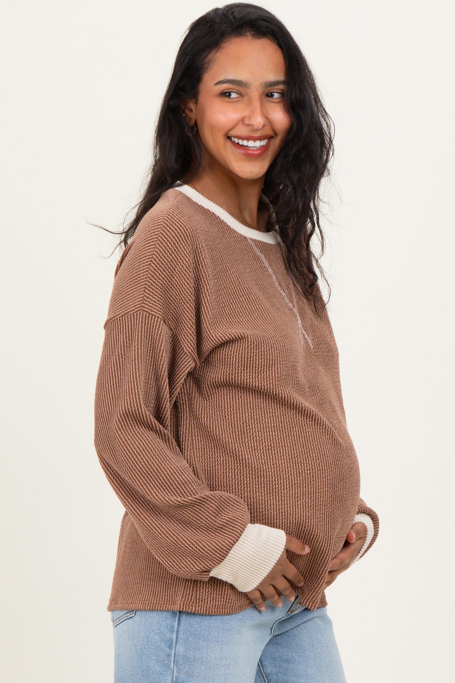 woman wearing a brown ribbed maternity sweater with light beige accents and a visible baby bump