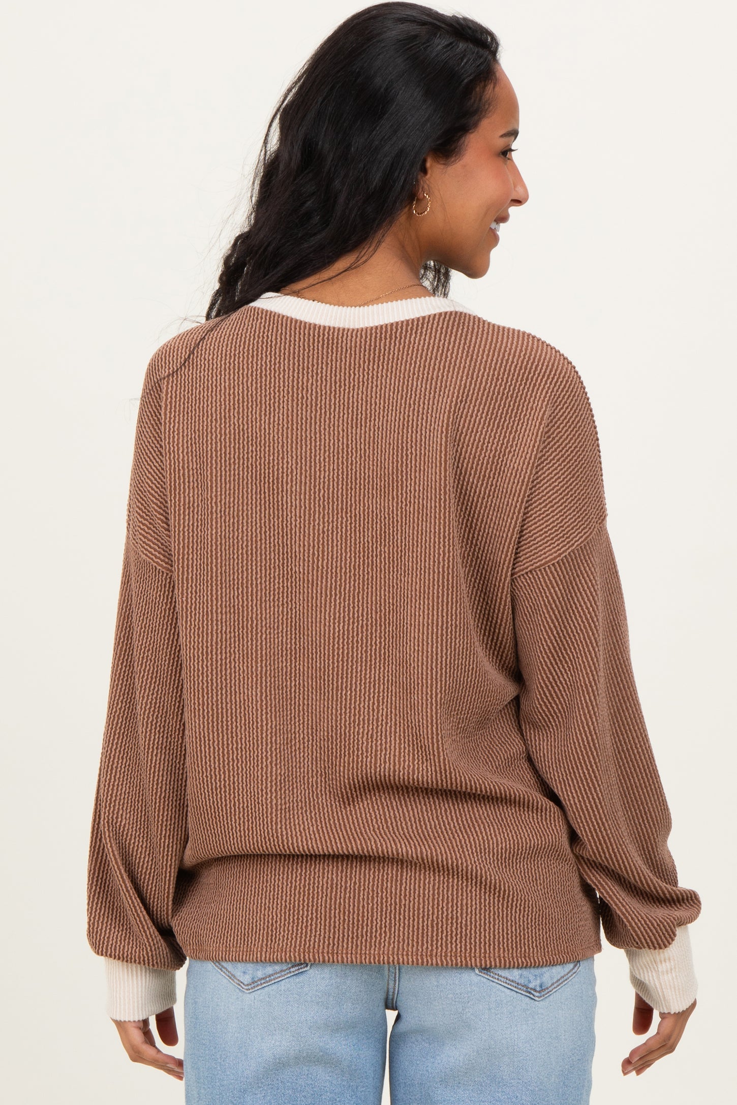 woman wearing a brown maternity sweater with contrast white cuffs, seen from the back with a relaxed fit