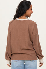 woman wearing a brown maternity sweater with contrast white cuffs, seen from the back with a relaxed fit