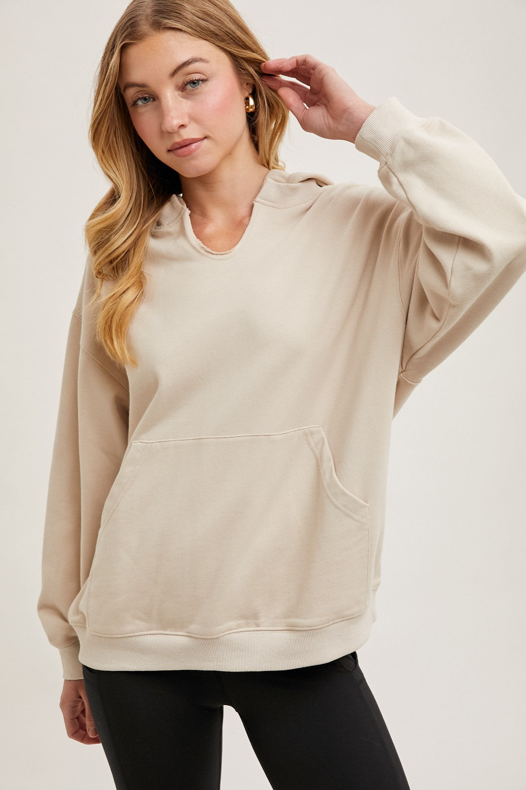 woman wearing a beige hooded sweatshirt with a front pocket and relaxed fit, styled with black leggings