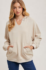 woman wearing a beige oversized hoodie with a v-neck and front pockets, styled with blue jeans