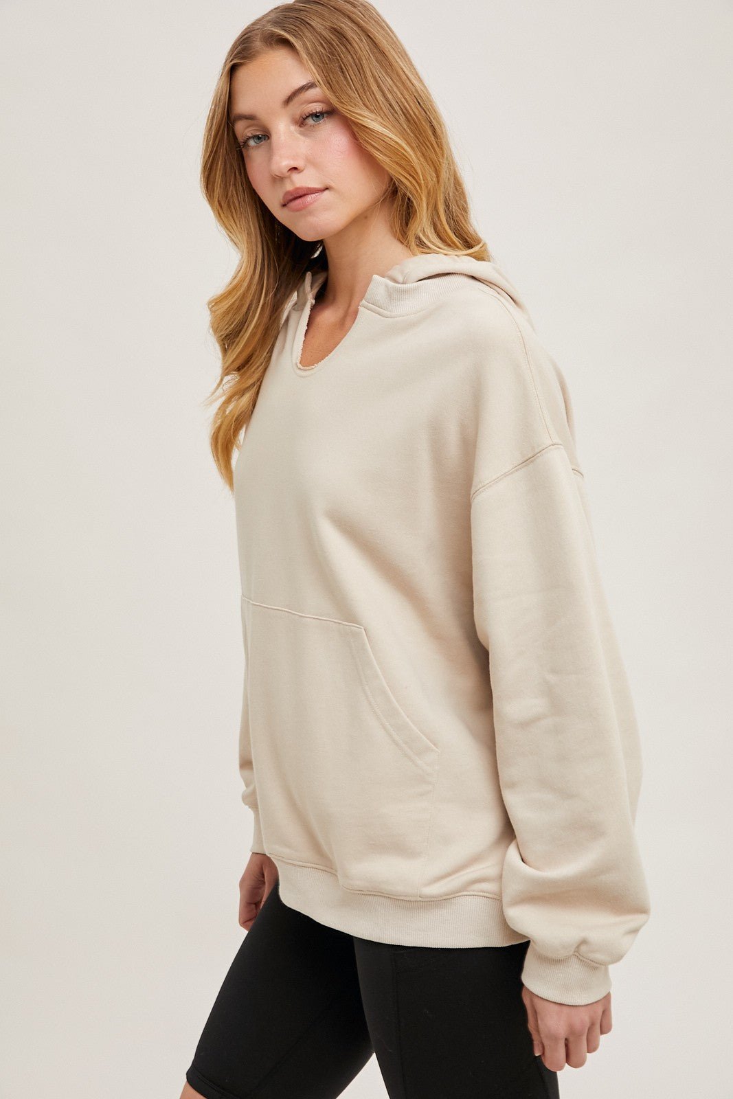 woman wearing a beige oversized hoodie with a front pocket and a drawstring hood, styled with black bike shorts
