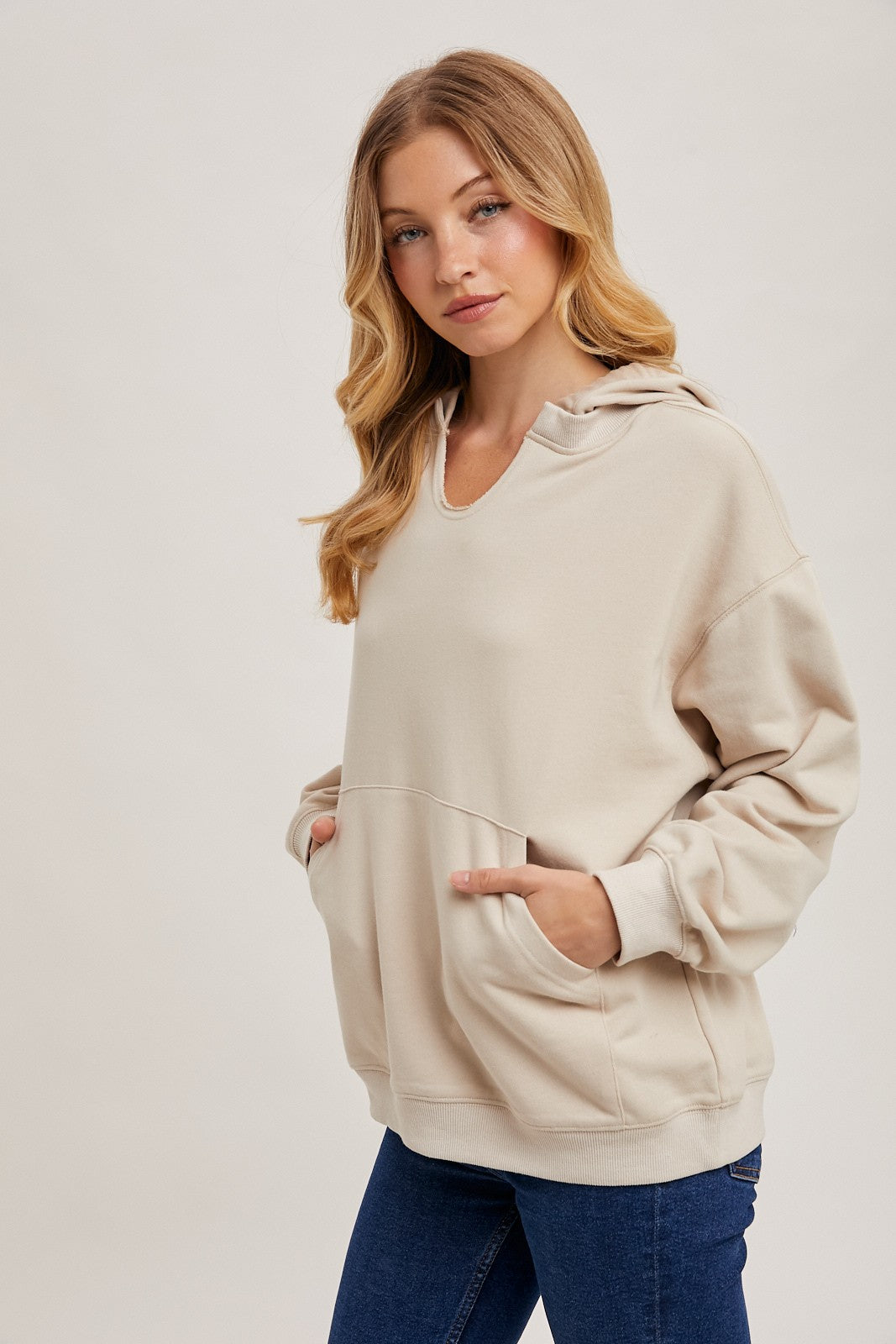 woman wearing a beige oversized hoodie with a front pocket and adjustable hood, paired with blue jeans