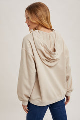 woman wearing a beige oversized hoodie with a back cutout and ribbed trim, styled with blue jeans