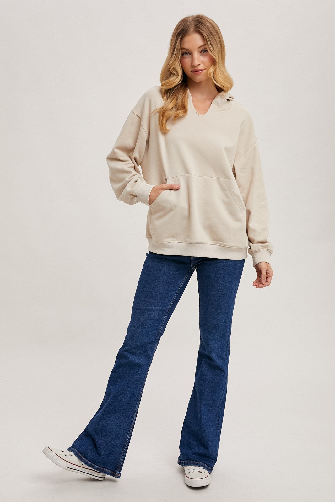woman wearing a beige oversized hoodie and flared jeans, standing with one hand in the pocket