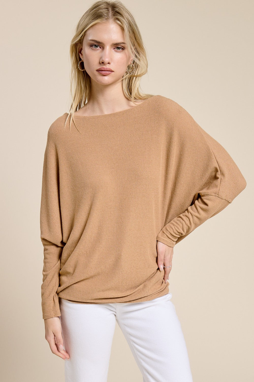 woman wearing a camel oversized long sleeve top with a boat neckline and relaxed fit paired with white jeans