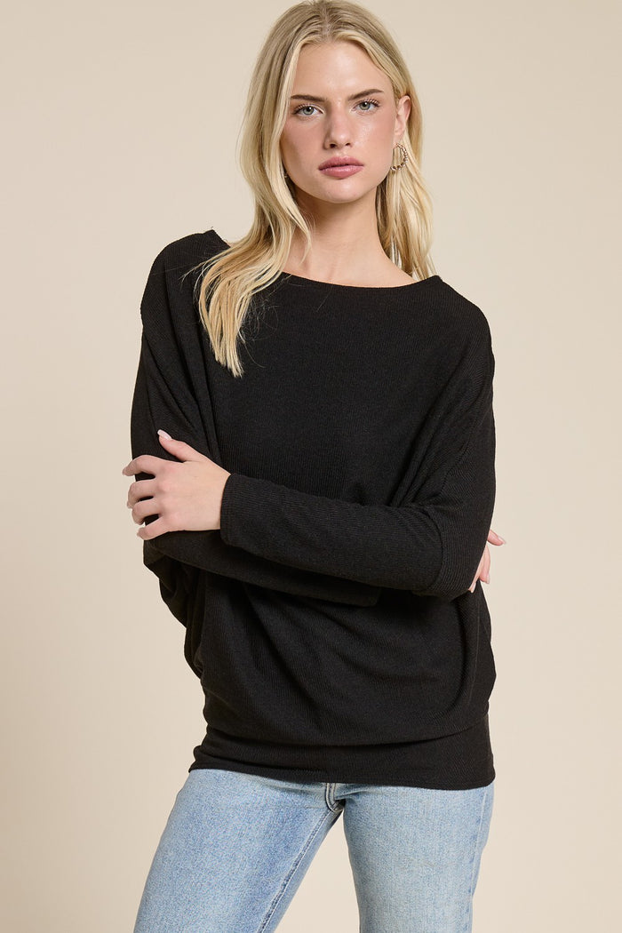 woman wearing a black oversized sweater with a wide neckline and relaxed fit, paired with light blue jeans