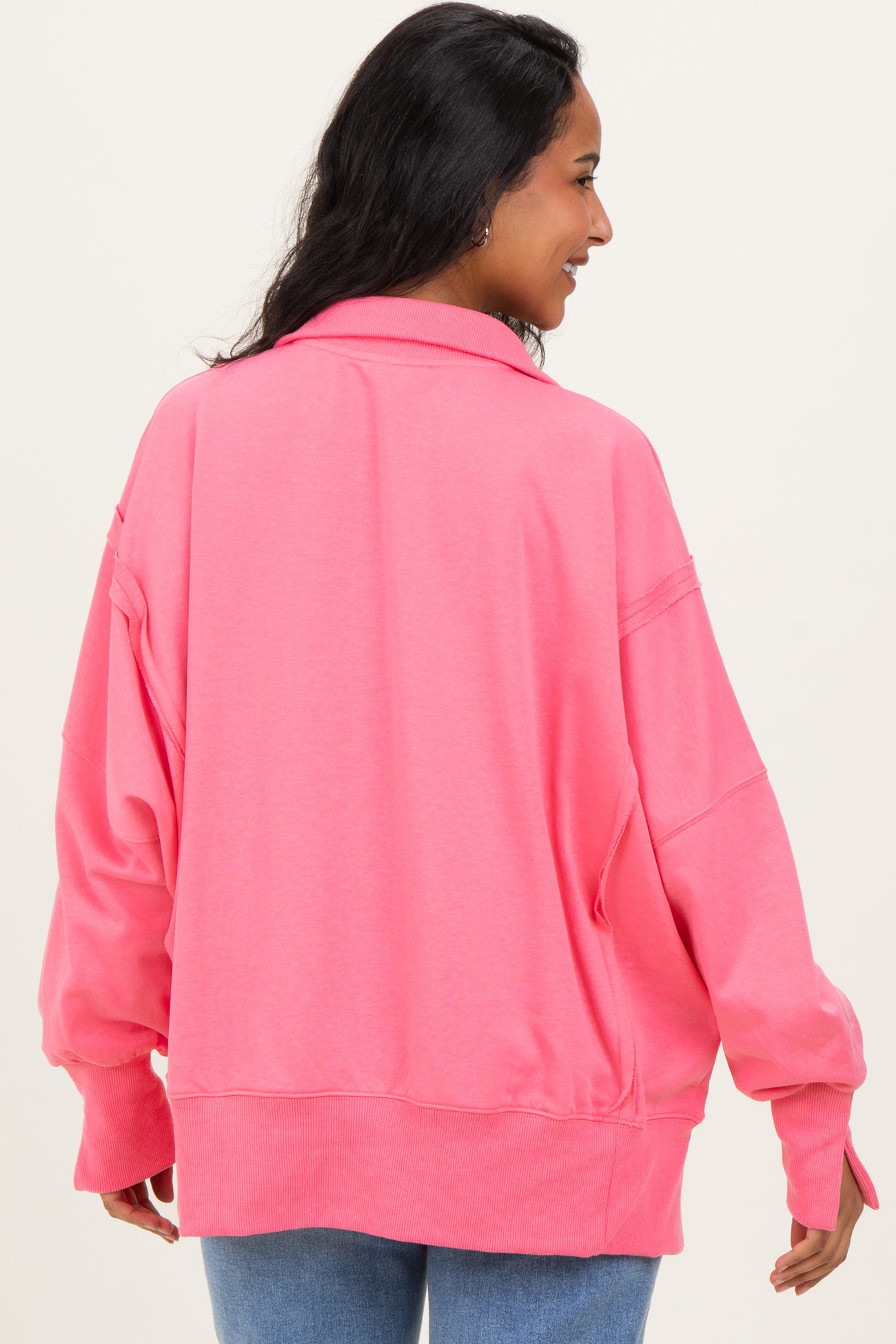woman wearing a bright pink oversized maternity sweatshirt, viewed from the back