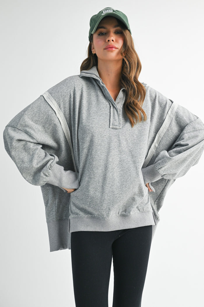 woman wearing an oversized gray pullover sweatshirt with a collared neck and ribbed cuffs, paired with black leggings