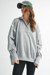 woman wearing a gray oversized pullover sweatshirt with a collared neckline and long sleeves, paired with black leggings and a green cap