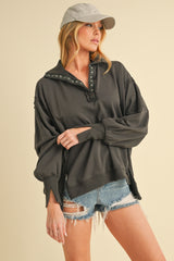 woman wearing a dark gray oversized sweatshirt with snap details and distressed denim shorts