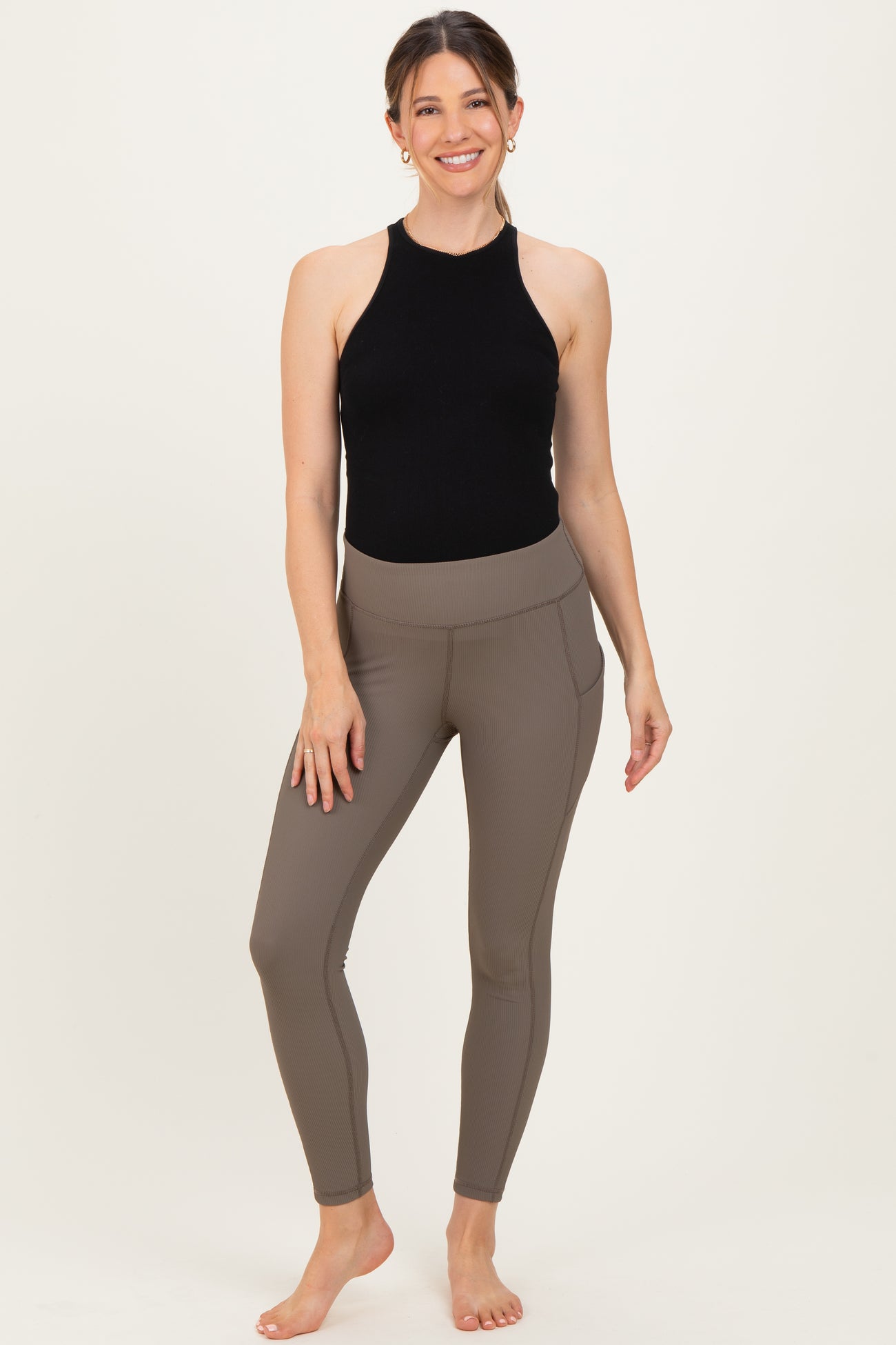 woman wearing a black halter neck maternity top and brown ribbed maternity leggings with side pockets