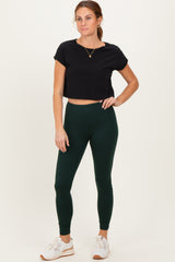 woman wearing a black cropped t-shirt and dark green leggings with white sneakers
