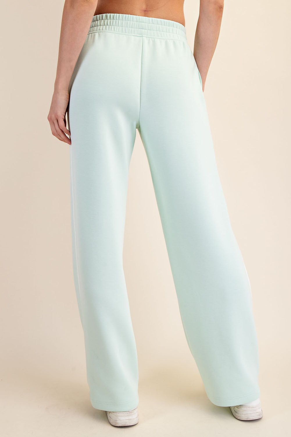 woman wearing light green wide-leg sweatpants, viewed from the back, featuring a comfortable elastic waistband
