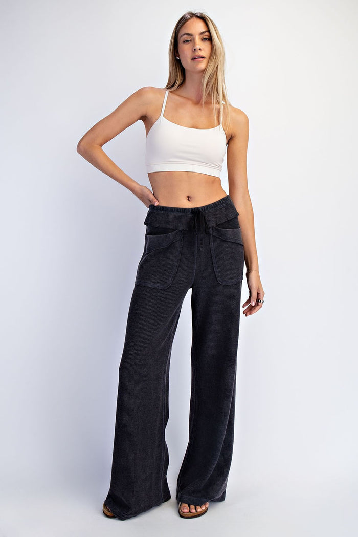 woman wearing a white crop top and black wide-leg pants with pockets, posing with one hand on her hip