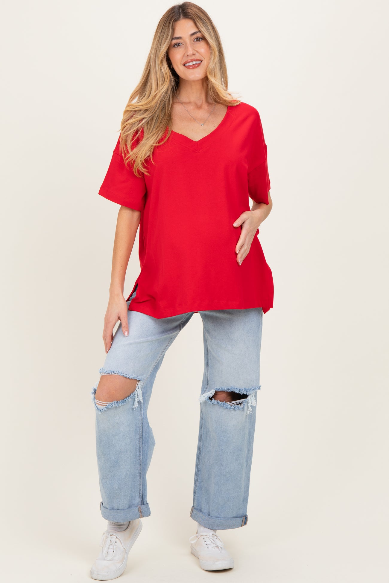 woman wearing a red v-neck maternity top and distressed light blue jeans, showing her baby bump