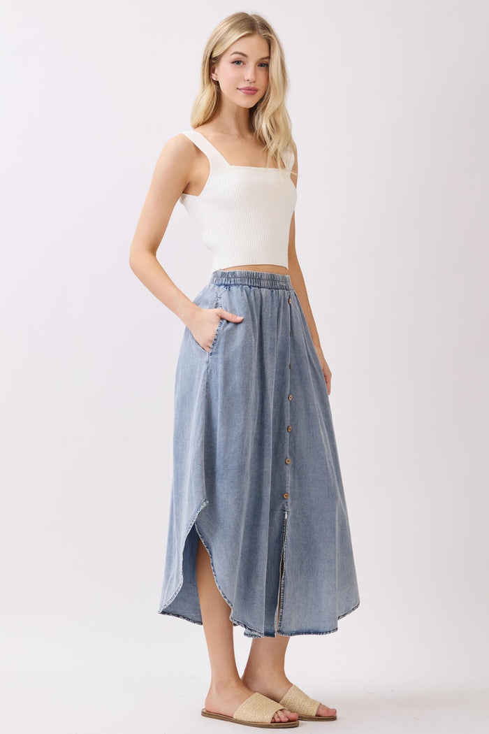 woman wearing a white ribbed crop top and a light blue button-up denim maxi skirt with pockets