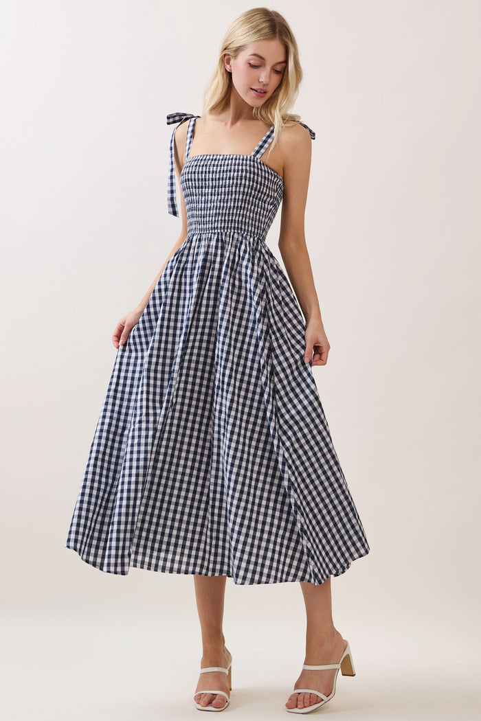 woman wearing a navy and white gingham midi dress with tie straps and a smocked bodice
