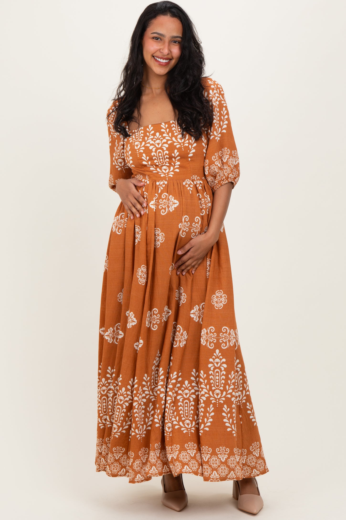 woman wearing an orange floral print maternity maxi dress and holding her baby bump