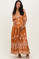 woman wearing an orange floral print maternity maxi dress and holding her baby bump