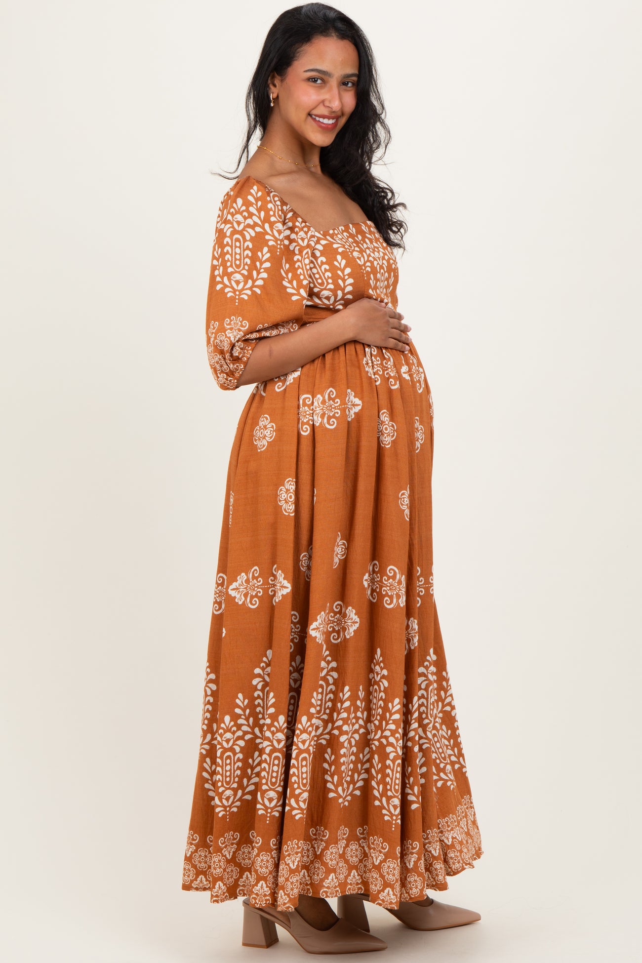 woman wearing a brown floral patterned maternity dress and holding her baby bump