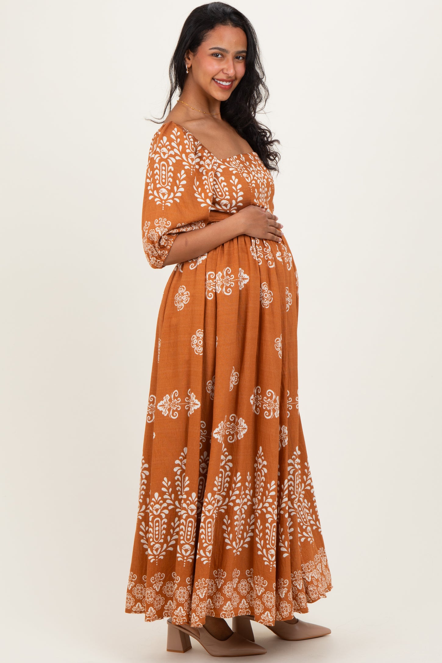 woman wearing a brown floral patterned maternity dress and holding her baby bump