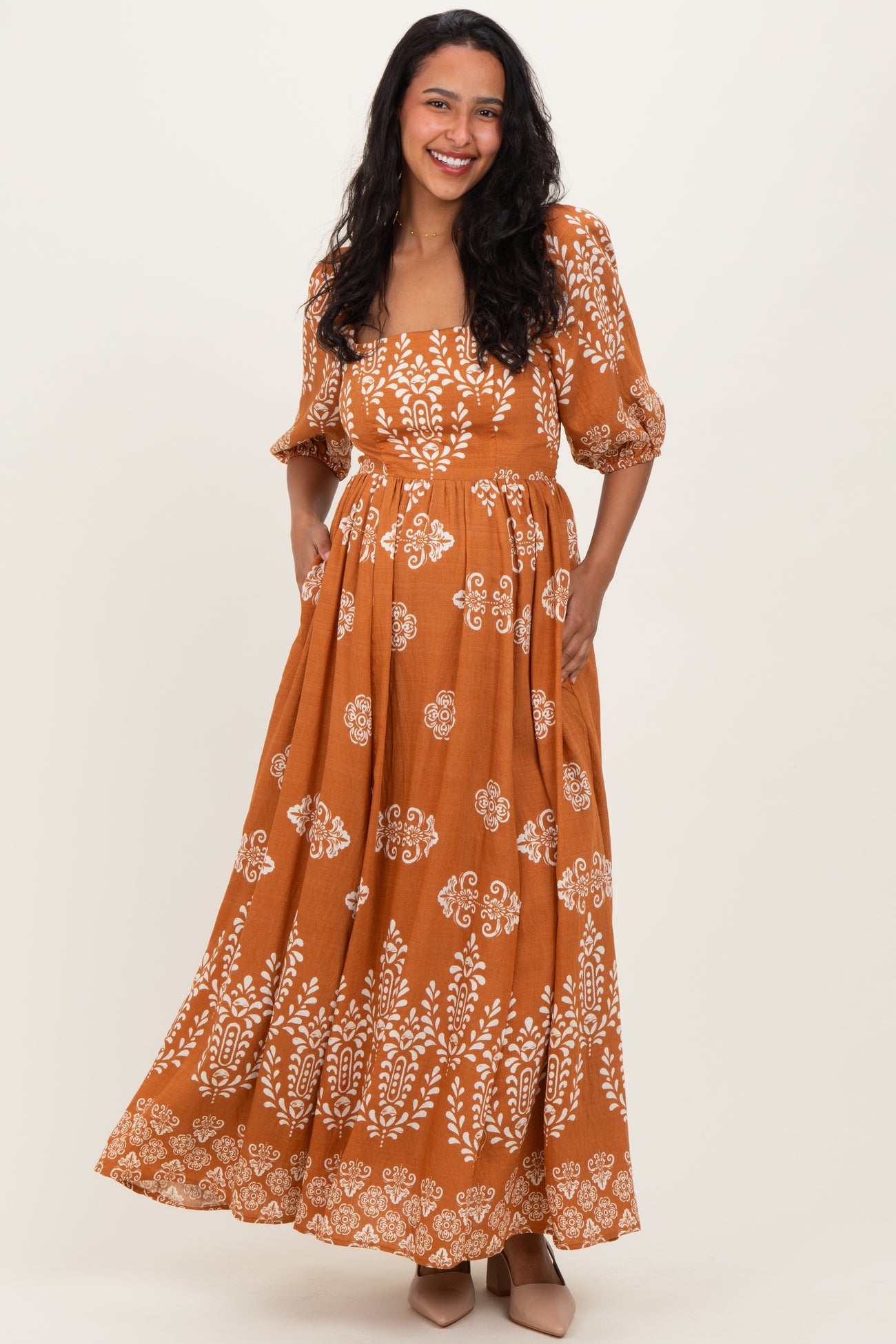 woman wearing an orange maternity maxi dress with white floral patterns and puff sleeves, showing her baby bump