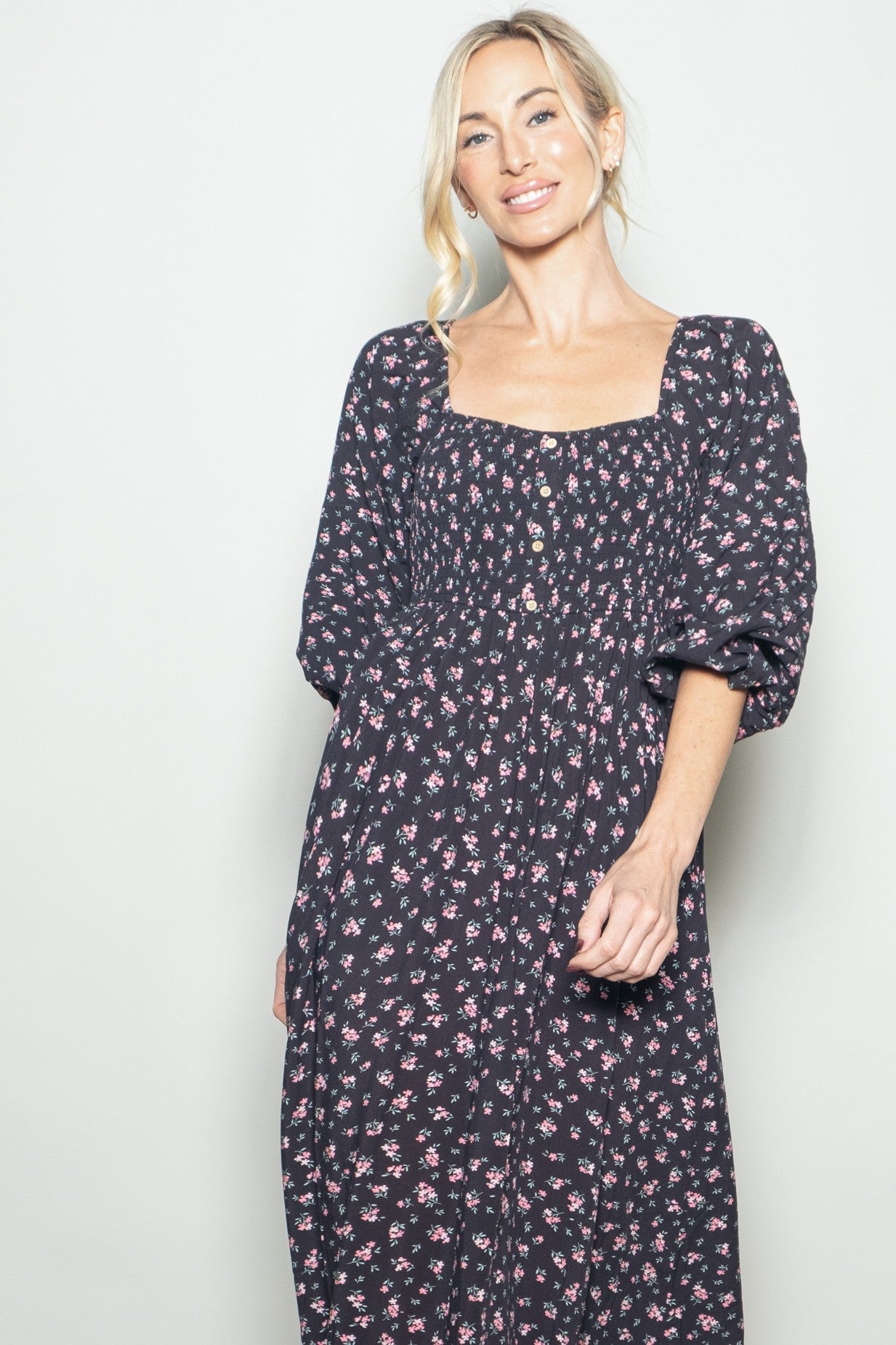 woman wearing a black floral maxi dress with puff sleeves and a square neckline, smiling at the camera