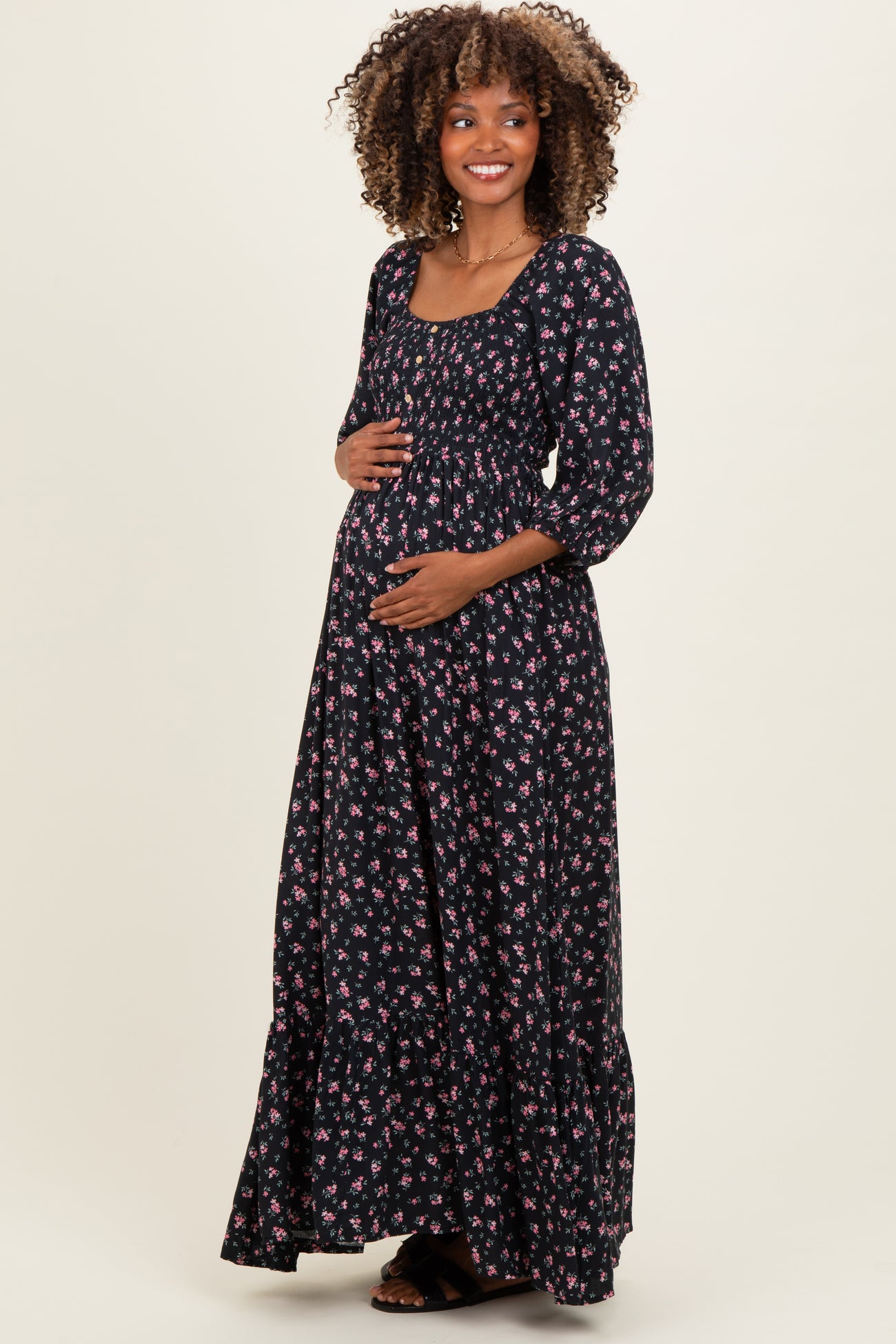 woman wearing a black floral maternity maxi dress with a square neckline and three-quarter sleeves, holding her baby bump