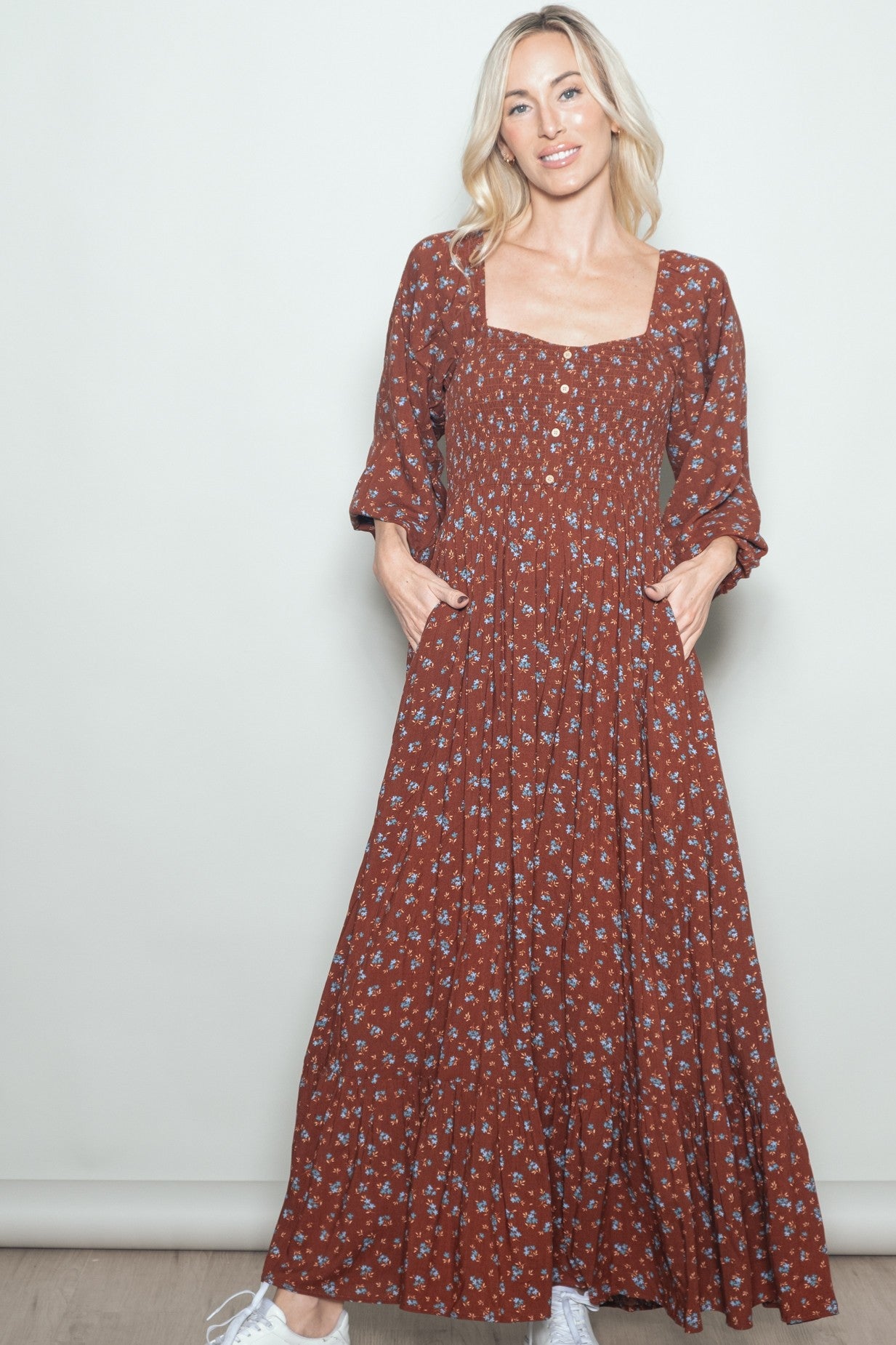 woman wearing a rust floral maxi dress with square neckline and pockets, styled with white sneakers