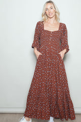 woman wearing a rust floral maxi dress with square neckline and pockets, styled with white sneakers