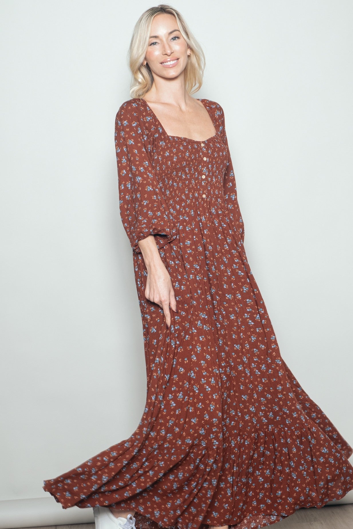 woman wearing a brown floral maxi dress with a square neckline and long sleeves, smiling and posing gracefully