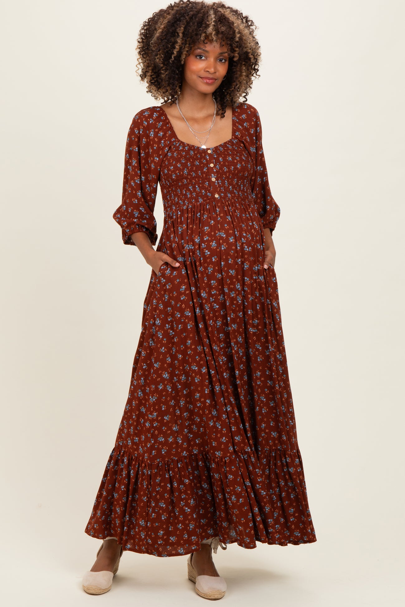 woman wearing a brown floral maternity maxi dress with pockets and balloon sleeves, showcasing her baby bump