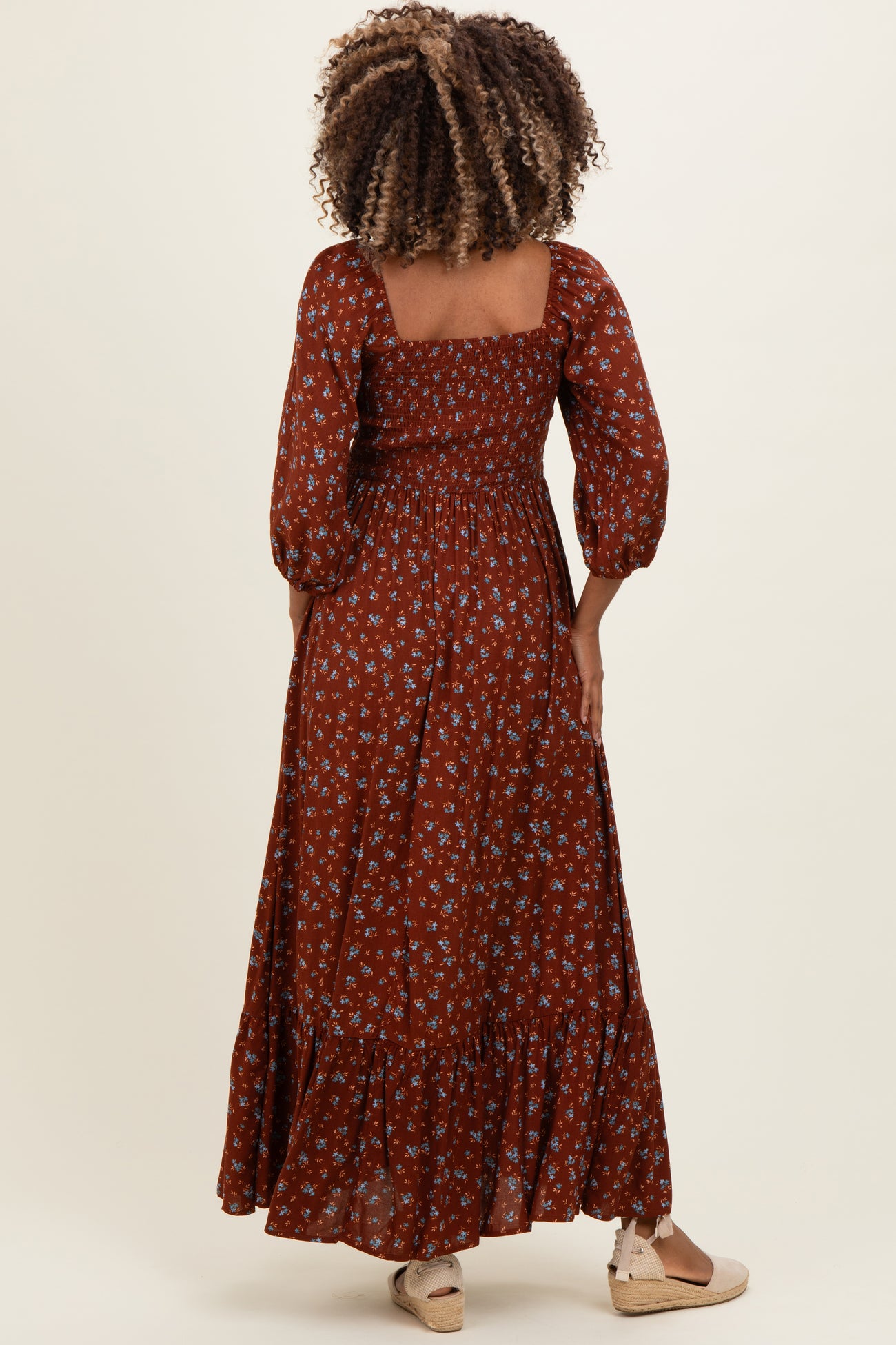 woman wearing a brown floral maternity maxi dress with puff sleeves and a smocked bodice, showing her baby bump from behind