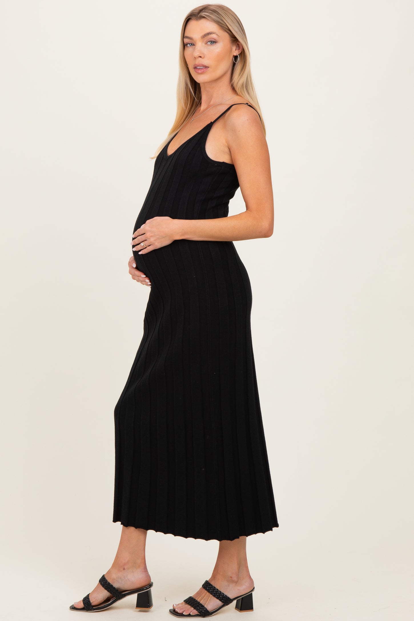 woman wearing a black ribbed maternity dress and cradling her baby bump
