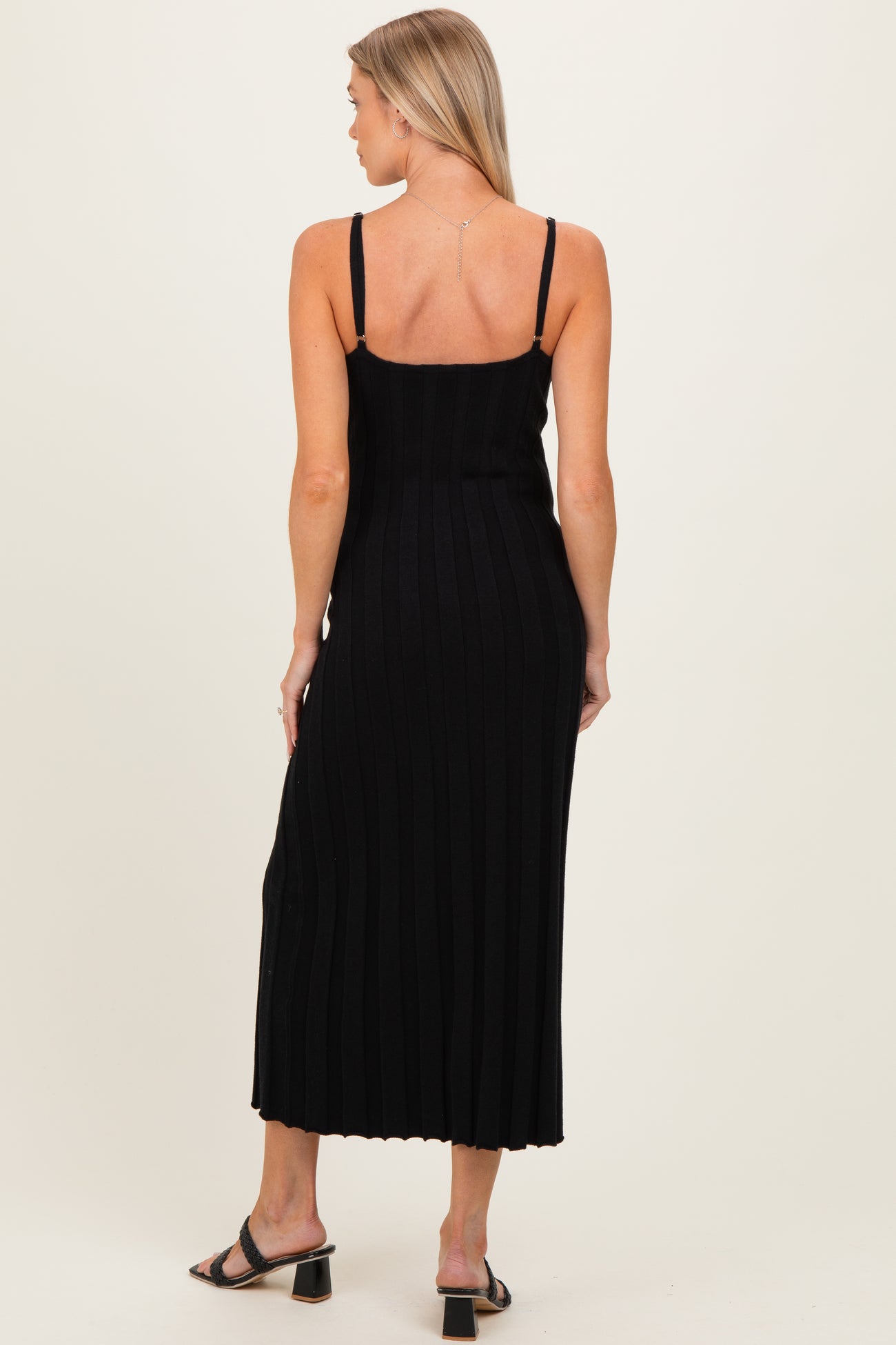 woman wearing a fitted black ribbed maternity dress with adjustable straps, showing a subtle back design