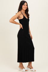 woman wearing a black ribbed maxi dress with thin straps and a fitted silhouette, posing sideways.
