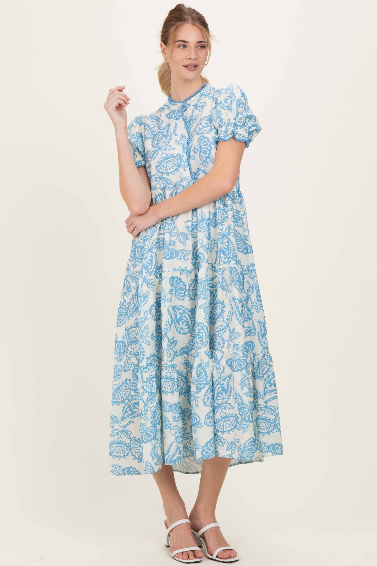 woman wearing a blue floral midi dress with puff sleeves and a high neckline, standing against a neutral background