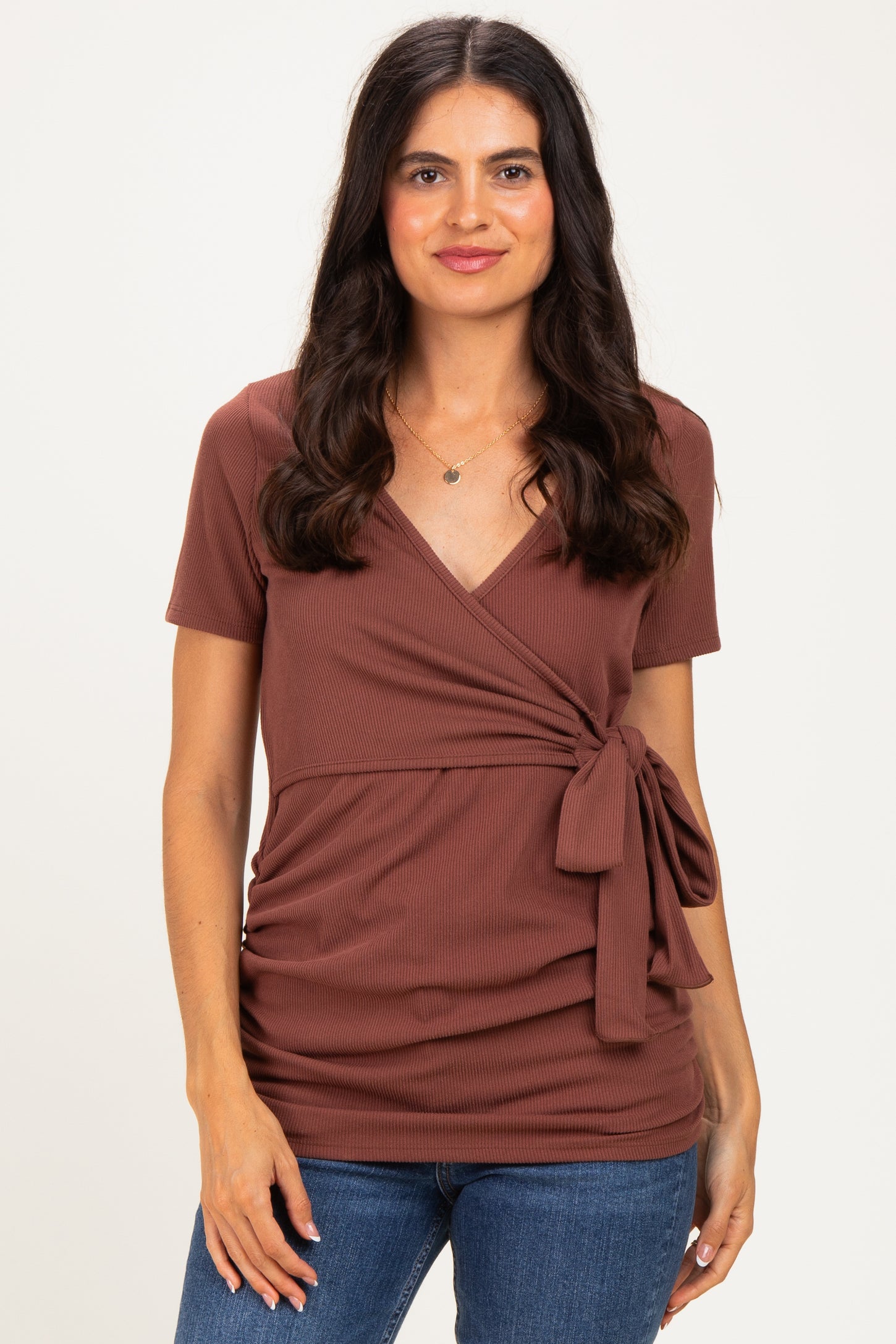 woman wearing a rust-colored short sleeve wrap top with a tie detail at the waist and jeans