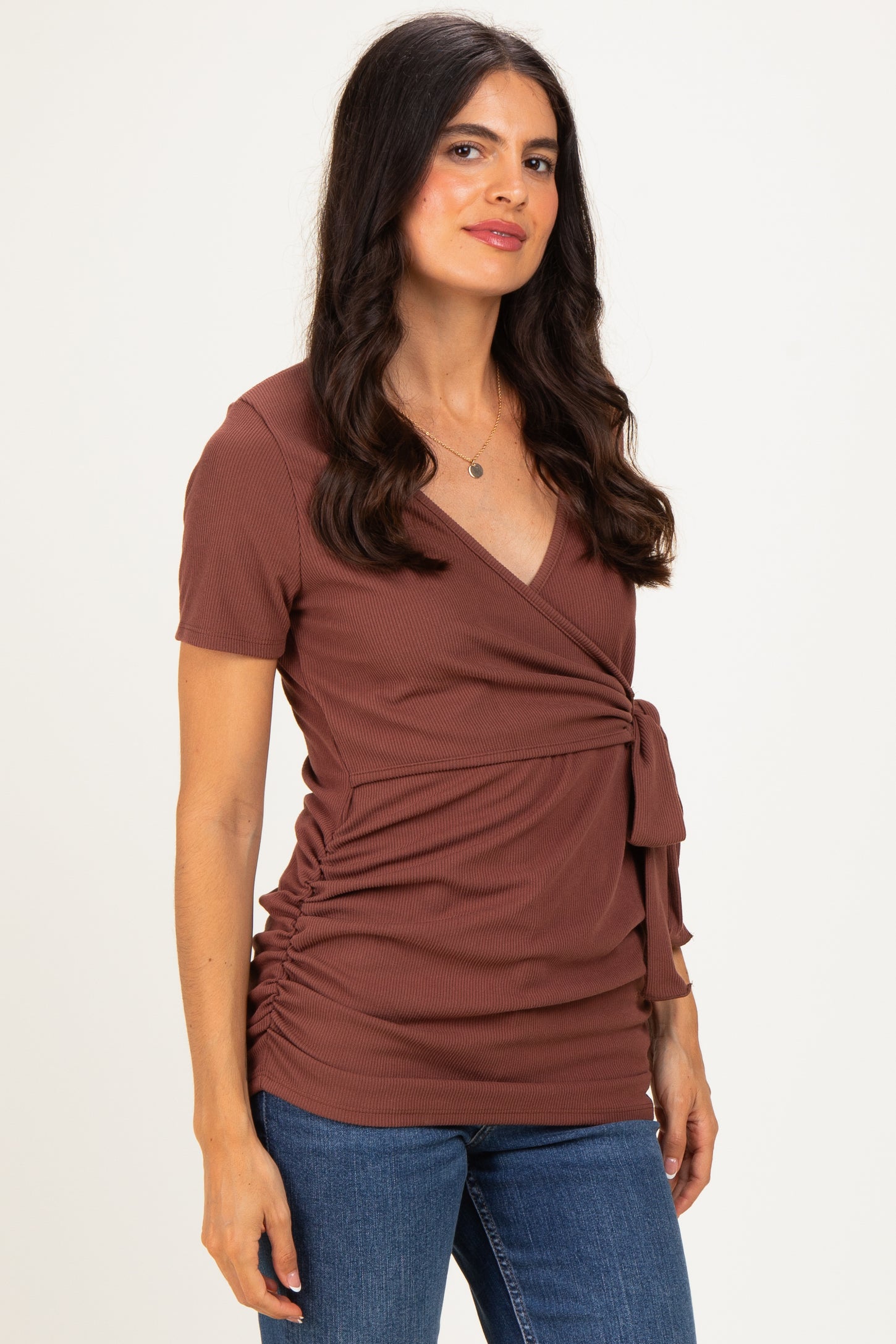 woman wearing a rust brown short sleeve wrap top with tie details and side ruching, paired with blue jeans