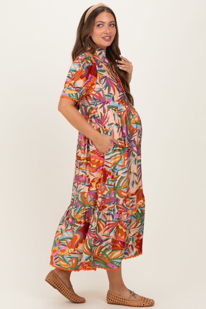 woman wearing a colorful floral print maternity dress with a tiered skirt and pockets, showcasing her baby bump