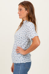 woman wearing a light blue short sleeve blouse with a floral pattern and scalloped edges, styled with jeans
