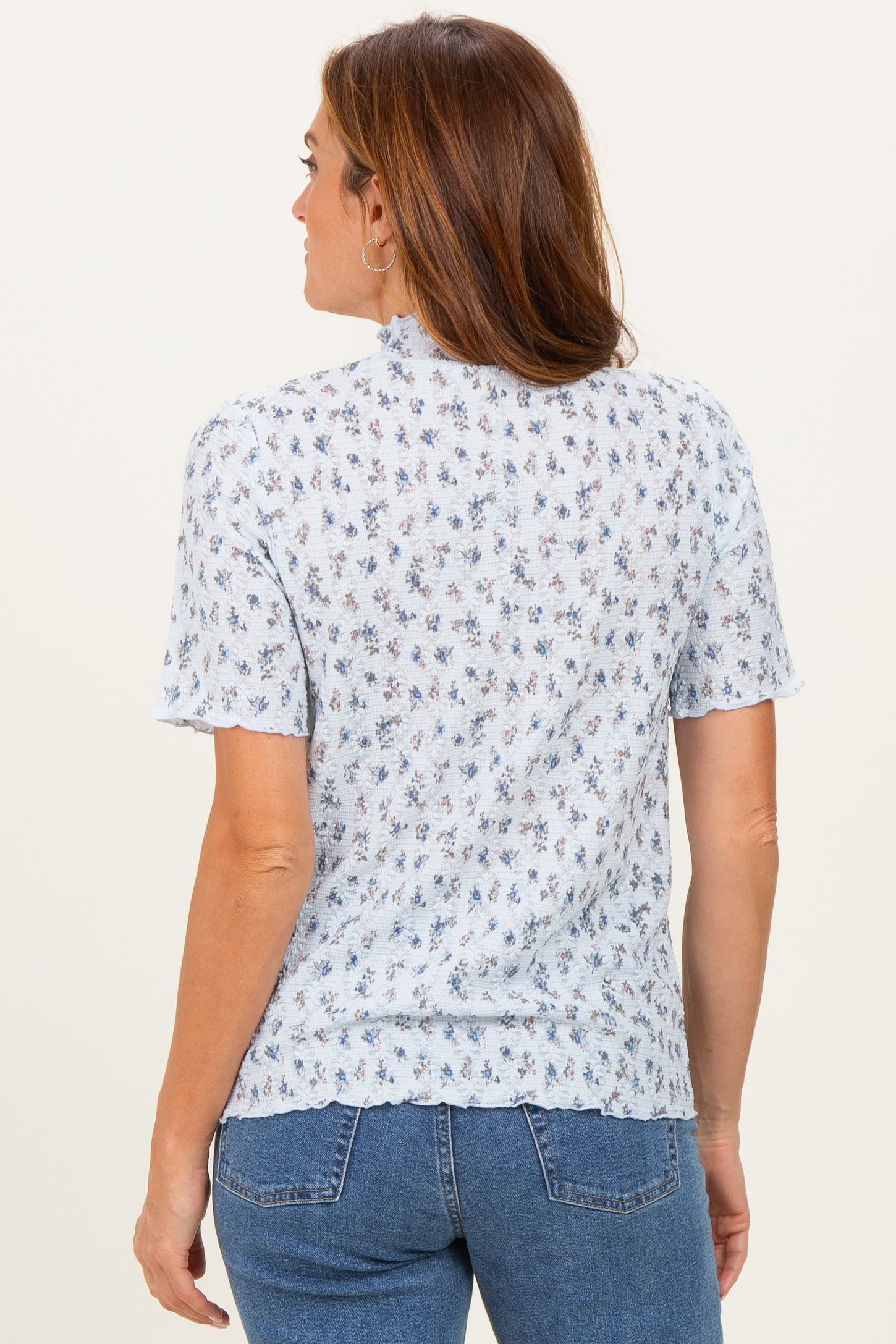 woman wearing a light blue short sleeve blouse with floral print and a back view, paired with denim jeans