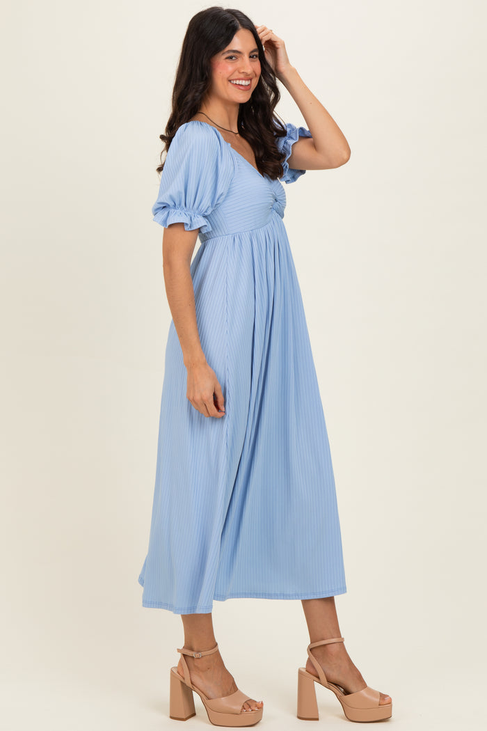 woman wearing a light blue maxi dress with puff sleeves and a cinched waist, standing on a neutral background