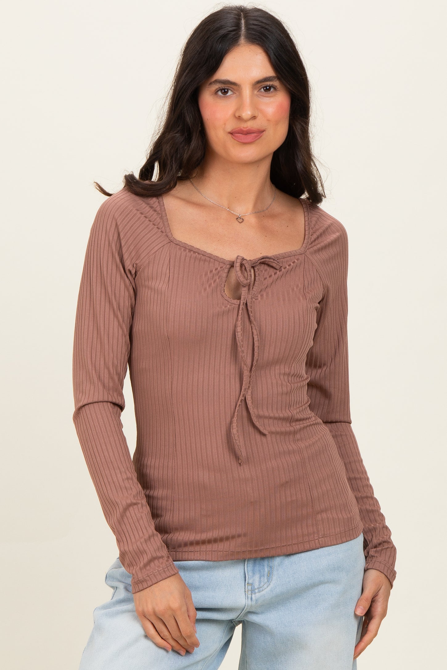 woman wearing a brown ribbed long sleeve top with a square neckline and tie detail, paired with light blue jeans