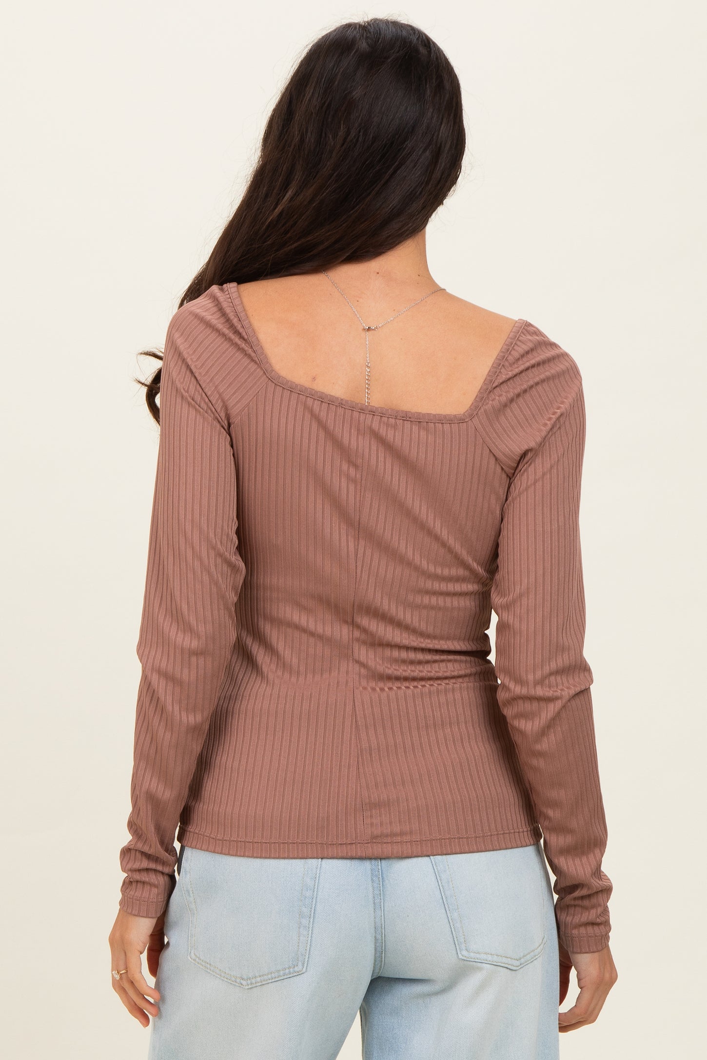 woman wearing a mauve ribbed long sleeve top with a square neck and gathered shoulder details, viewed from the back