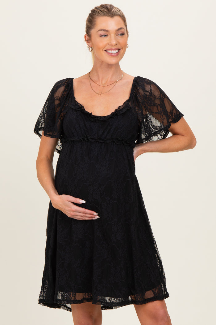 woman wearing a black lace maternity dress with short flutter sleeves and holding her baby bump