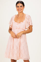 woman wearing a soft pink lace dress with flutter sleeves and a tie waist, smiling at the camera