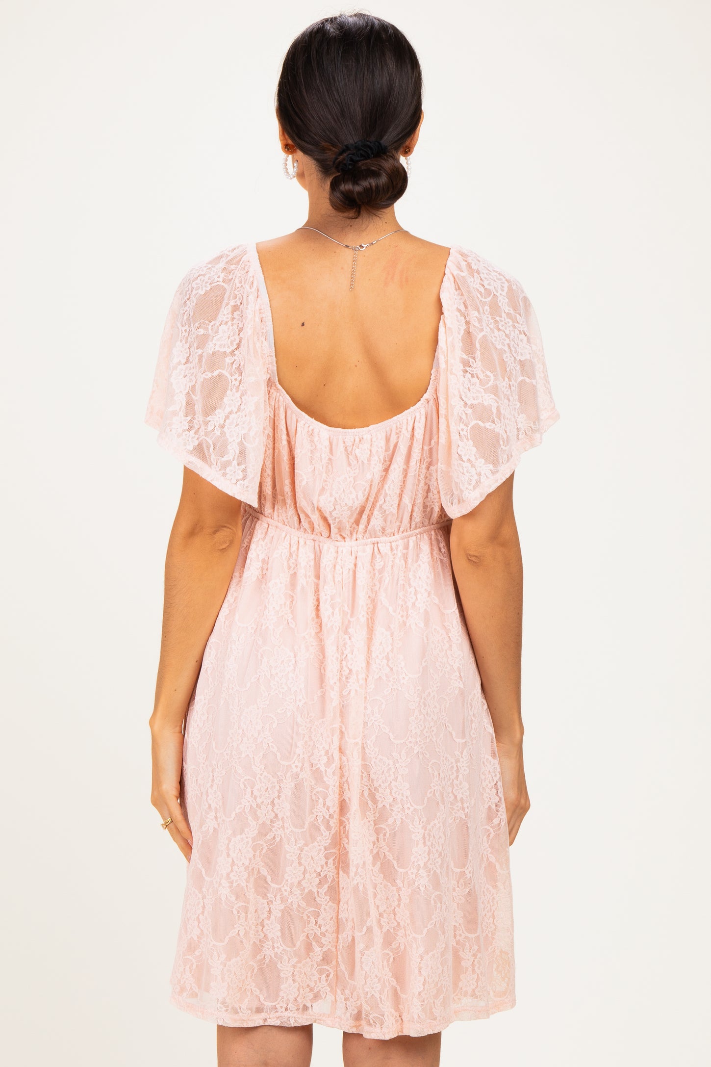 woman wearing a light pink lace dress with flutter sleeves and cinched waist, shown from the back